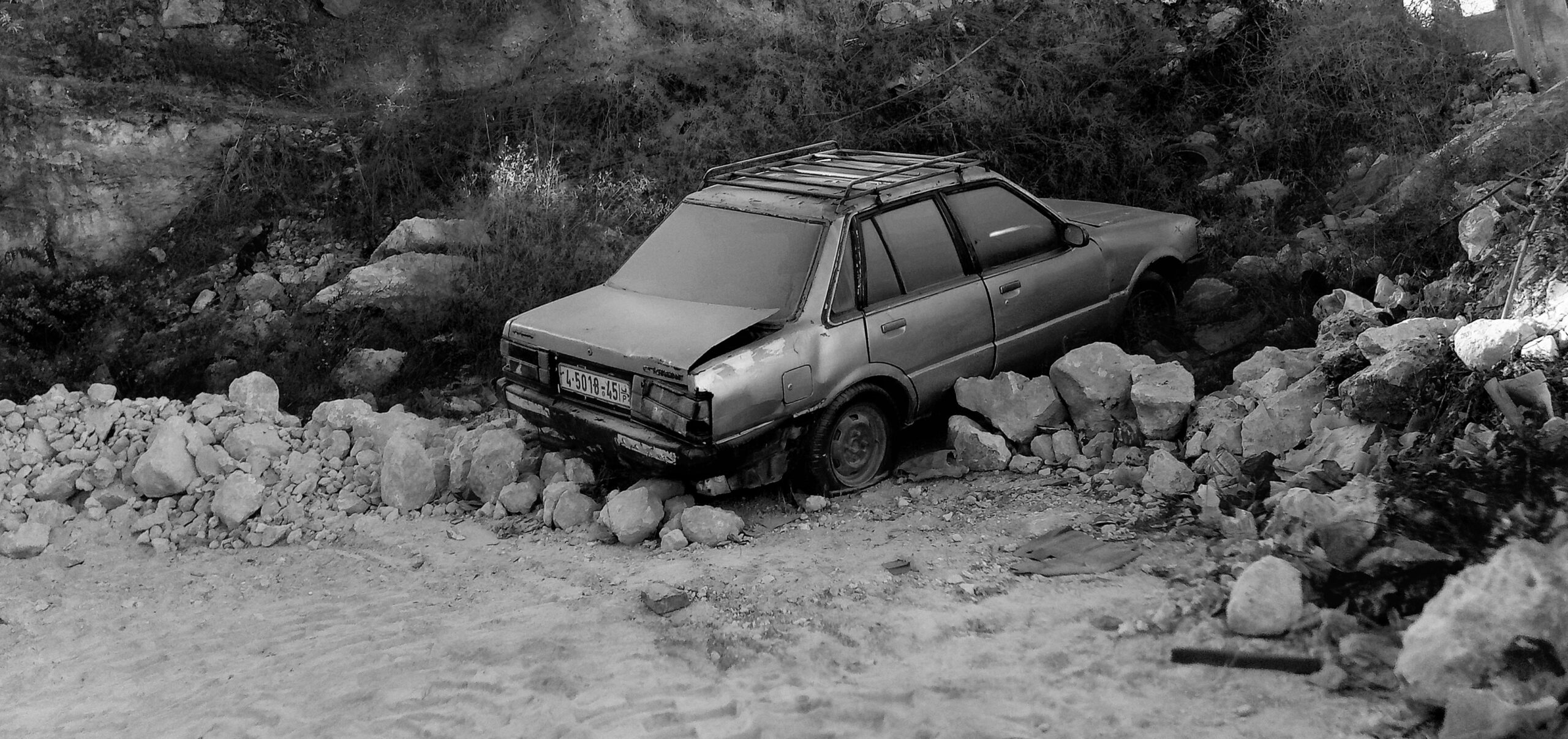 black and white photo of car crashed in the midst of rocks and rubble